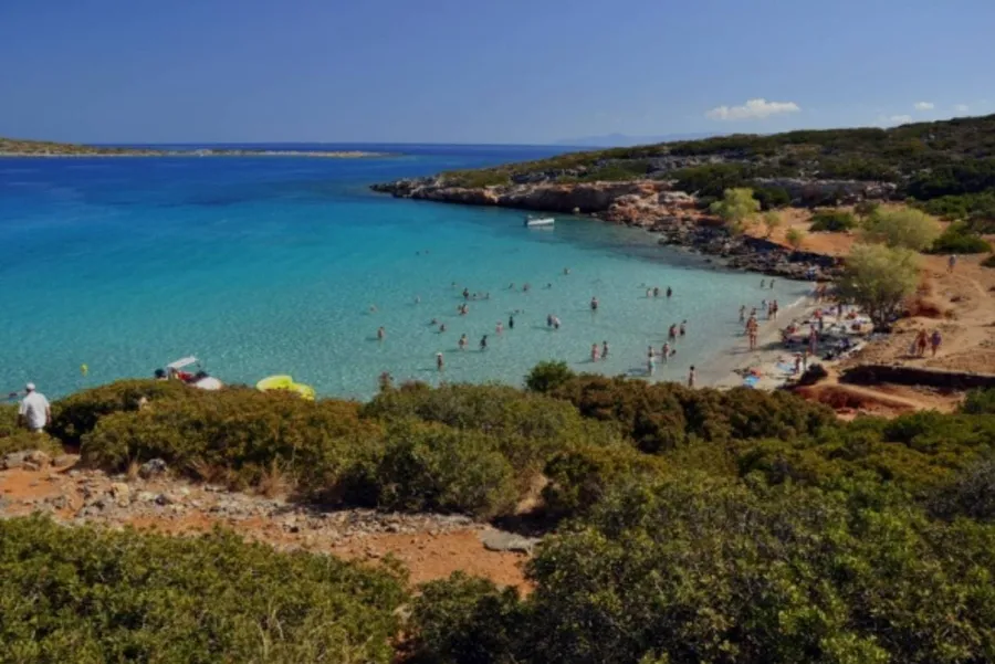 Small sandy bay with bright blue water and swimmers at Kolokytha Beach